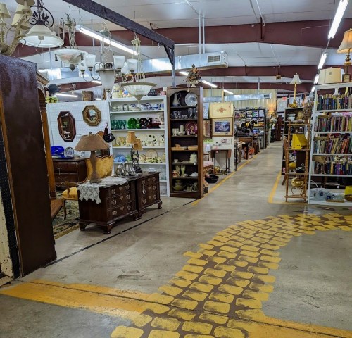A spacious antique store aisle lined with shelves of vintage items, furniture, and decorative pieces.