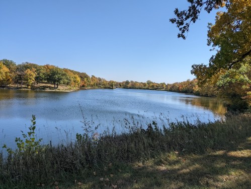 A serene lake surrounded by trees with autumn foliage under a clear blue sky.