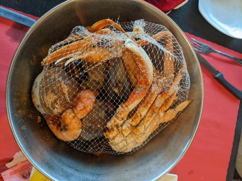 A metal bowl filled with seafood, including crabs and shrimp, covered with a netting.