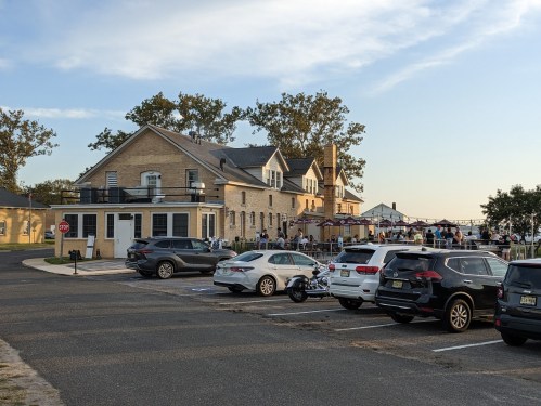A lively outdoor gathering at a historic building, with parked cars and people enjoying the evening.
