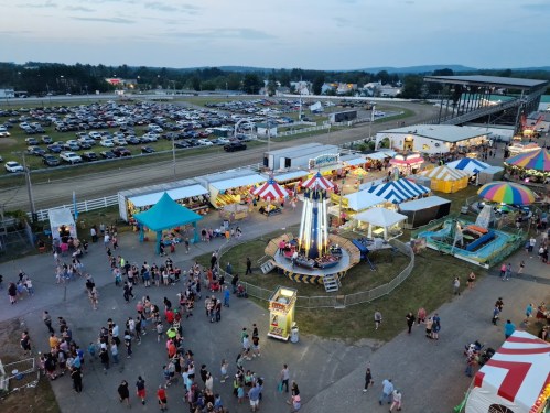 Aerial view of a lively fairground with rides, colorful tents, and a large crowd enjoying the festivities.