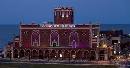 Historic building at Asbury Park, illuminated at dusk with "Greetings from Asbury Park" sign and ocean in the background.
