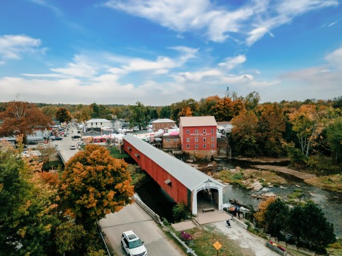 A scenic view of a covered bridge over a river, surrounded by autumn trees and a small town in the background.