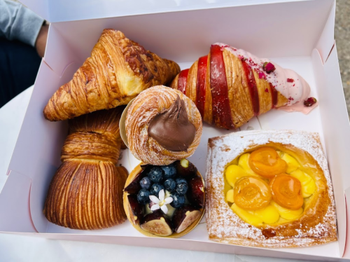 A box filled with assorted pastries, including croissants, a fruit tart, and a cream-filled pastry.