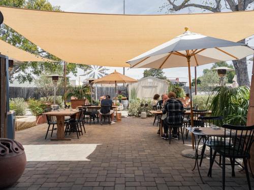 Outdoor dining area with shaded tables, umbrellas, and greenery, creating a relaxed atmosphere.