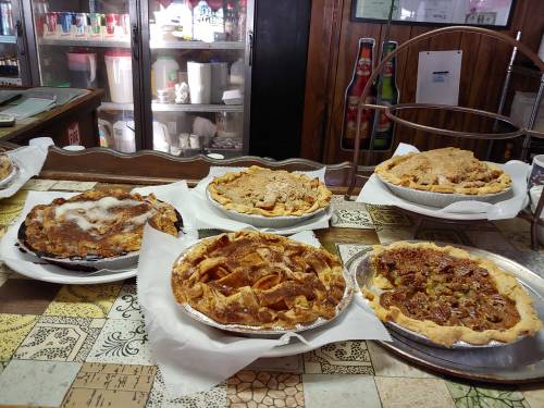 A variety of pies displayed on a table, including fruit and savory options, in a cozy setting.