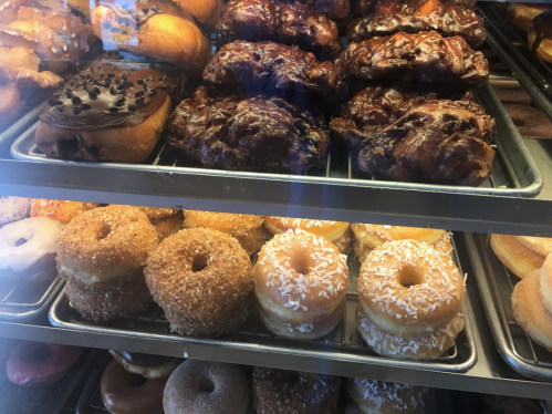 A display of assorted donuts, including glazed, chocolate, and topped varieties, arranged on trays.