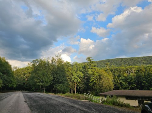 A scenic view of a road lined with trees, leading to a mountain under a partly cloudy sky.