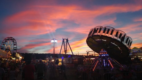 Colorful sunset over a carnival, featuring rides and bright lights, with people enjoying the festive atmosphere.