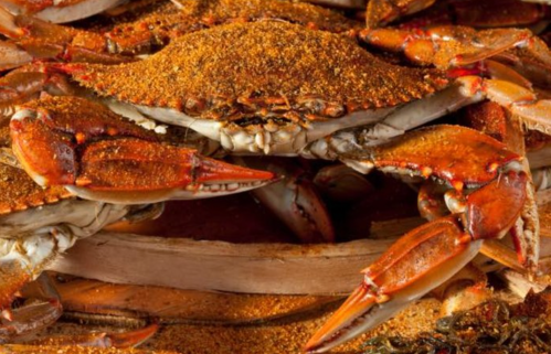 A close-up of crabs piled together, coated in a layer of seasoning, resting in a wooden container.