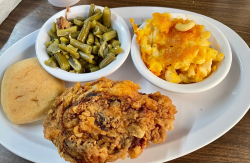 A plate with fried chicken, macaroni and cheese, green beans, and a roll.