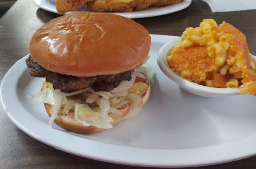 A hamburger with lettuce on a bun, served with a side of macaroni and cheese on a white plate.