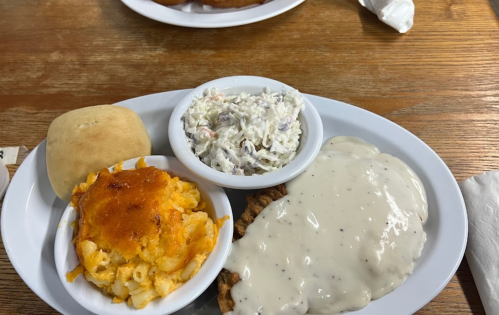 A plate of comfort food featuring fried chicken with gravy, macaroni and cheese, coleslaw, and a roll.