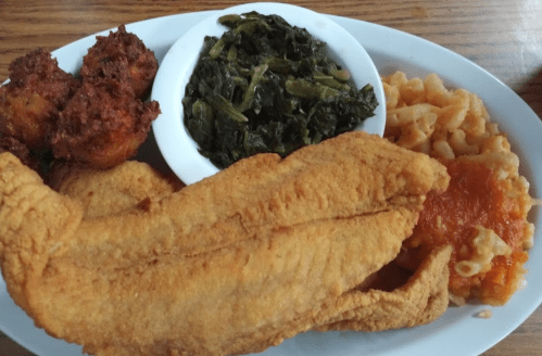 A plate of fried fish, macaroni and cheese, collard greens, and cornbread muffins.