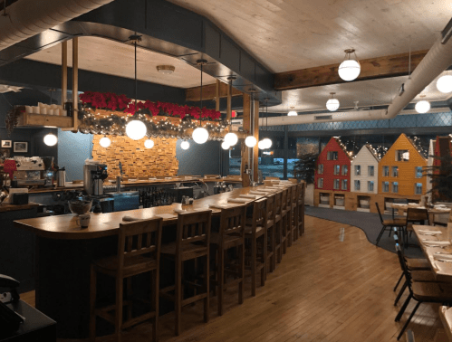 Cozy restaurant interior with a bar, wooden seating, festive decorations, and colorful house-shaped displays.