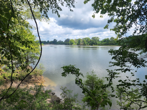 A serene lake surrounded by lush greenery and trees under a partly cloudy sky.