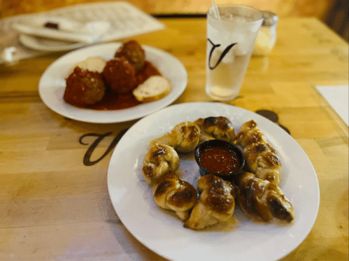 A plate of golden-brown stuffed knots with marinara sauce, alongside a plate of meatballs in red sauce.