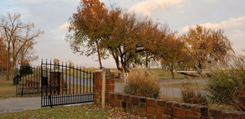 A scenic view of a gated entrance with trees and autumn foliage, set against a cloudy sky.