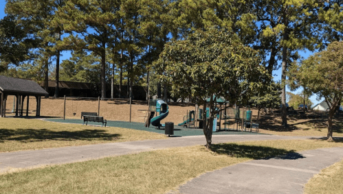 A sunny park scene featuring a playground with slides, benches, and trees in the background.