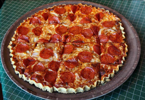 A large pepperoni pizza with a thick crust, cut into square slices on a round tray.