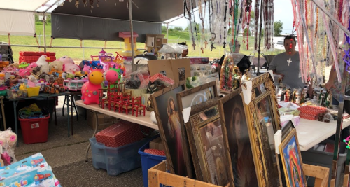 A bustling outdoor market stall filled with toys, decorations, and framed art, with a vendor in the background.
