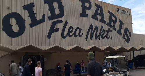 Exterior of Old Paris Flea Market with people walking in front and a sign indicating open hours on weekends.