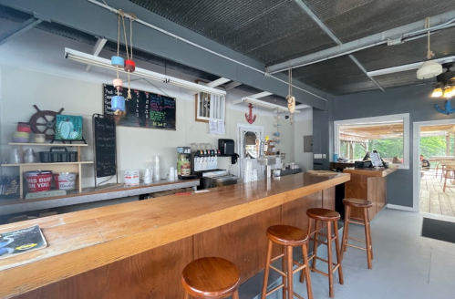 A cozy café interior with a wooden counter, stools, and a chalkboard menu, featuring nautical decor and natural light.