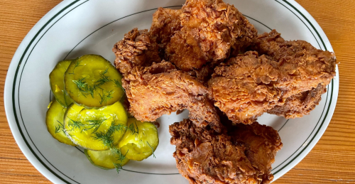 A plate of crispy fried chicken pieces served with sliced pickles and dill.