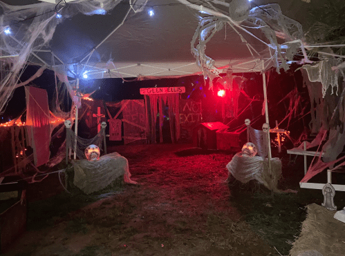 A spooky outdoor Halloween scene with cobwebs, glowing lights, and eerie decorations under a tent at night.