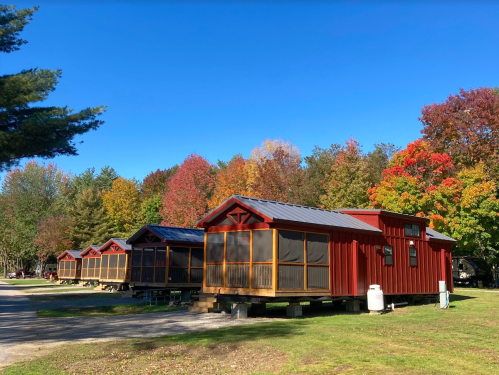 Row of red cabins with screened porches, surrounded by colorful autumn trees under a clear blue sky.