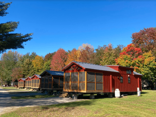 Row of red cabins with screened porches, surrounded by colorful autumn trees under a clear blue sky.