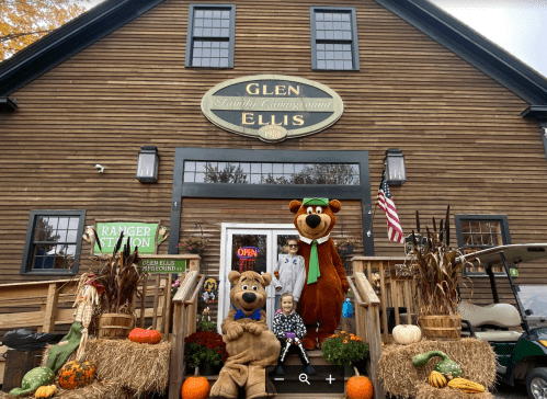 A family poses with two bear mascots outside a rustic building decorated for fall, featuring pumpkins and autumn decor.