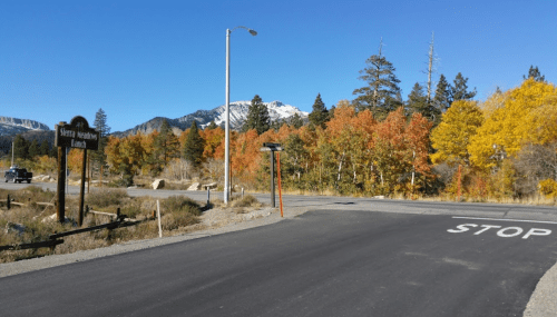 A scenic road intersection with autumn foliage, mountains in the background, and a clear blue sky.