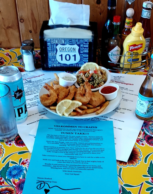 A colorful table setting with a plate of shrimp, pasta salad, drinks, and a welcome note at a restaurant in Oregon.