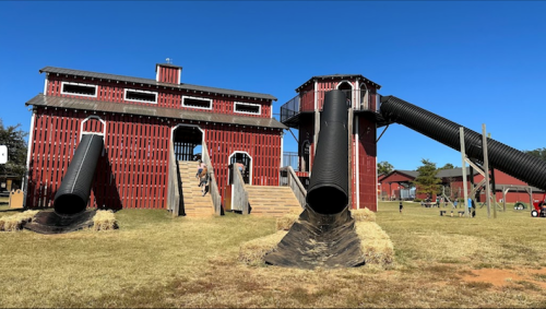 A large red barn structure with two black slides, set in a grassy area under a clear blue sky.