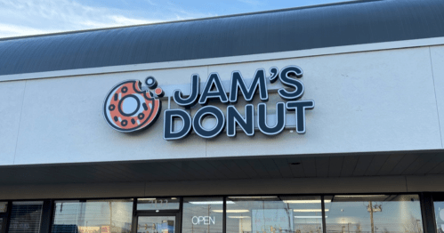 Sign for "Jam's Donut" with a donut graphic, located on a storefront. The shop is open.