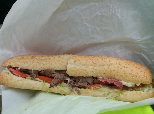 A sub sandwich filled with sliced beef, lettuce, tomatoes, and mayonnaise, served in a sesame seed bun.