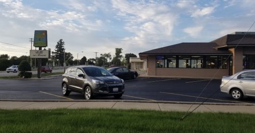 A gray SUV parked in front of a commercial building with a sign, under a partly cloudy sky.