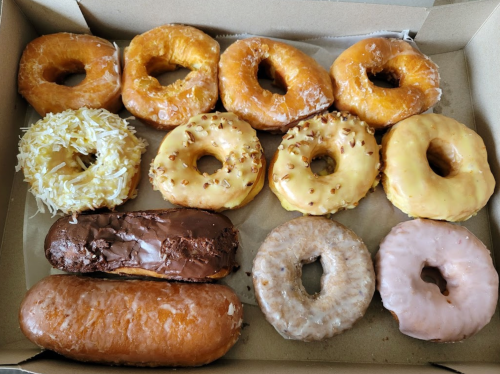 A box of assorted donuts, including glazed, chocolate, and frosted varieties, arranged in two rows.