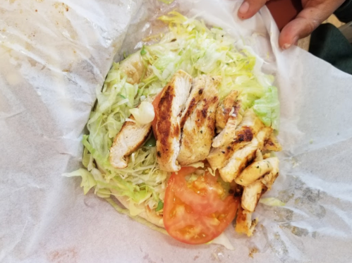 A close-up of a wrap filled with grilled chicken, lettuce, and tomato, partially wrapped in paper.