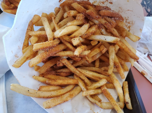 A large serving of golden-brown French fries sprinkled with seasoning, piled in a paper tray.