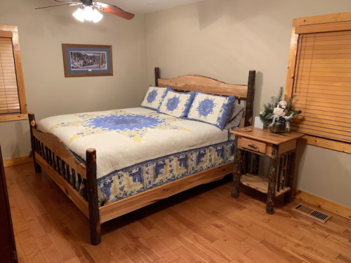 Cozy bedroom featuring a wooden bed with a blue and white quilt, nightstand, and warm wooden accents.