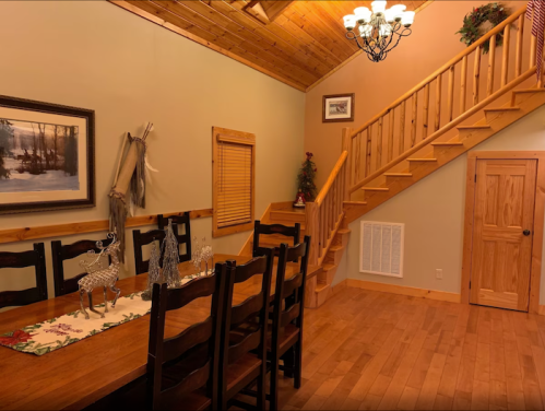 Cozy dining area with a wooden table, chairs, and a staircase leading to an upper level in a rustic cabin.