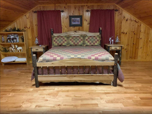 Cozy wooden bedroom with a quilted bed, rustic decor, and warm wooden walls and flooring.