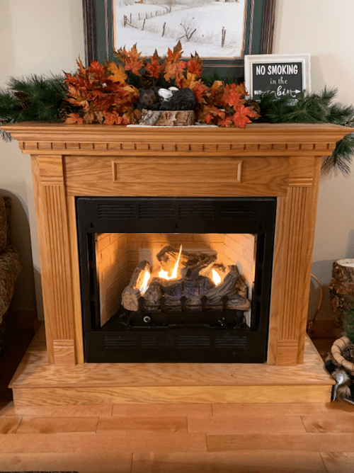 Cozy fireplace with autumn decor, surrounded by greenery and a sign that reads "No Smoking in the House."