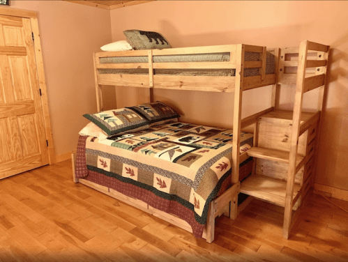 A wooden bunk bed with a lower double bed, adorned with a patterned quilt, in a cozy room with wooden walls.
