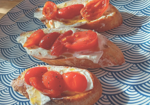 Three toasted bread slices topped with creamy cheese and roasted cherry tomatoes on a patterned blue plate.