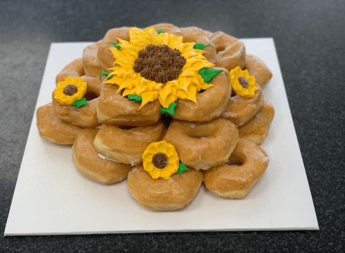 A decorative cake made of donuts arranged in a sunflower shape, topped with yellow frosting and chocolate center.