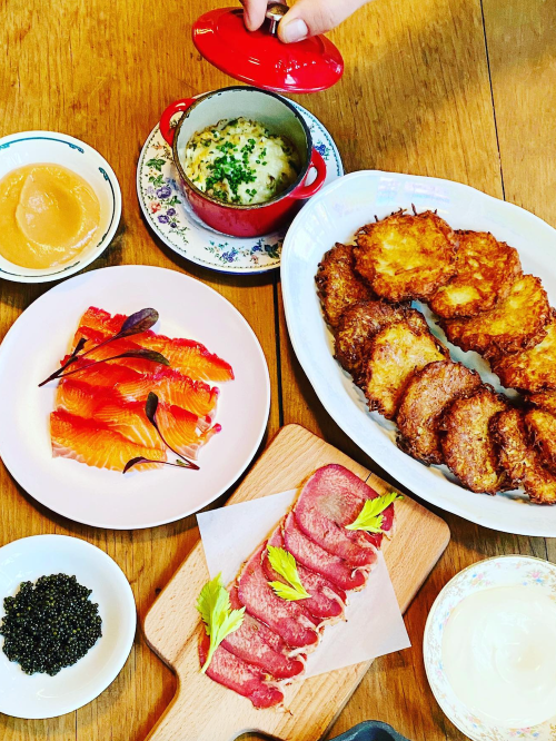 A table spread featuring latkes, smoked salmon, caviar, sour cream, and a small dish of creamy dip.