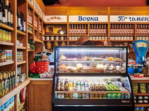 A cozy shop interior featuring shelves of bottles and jars, with a display case filled with various foods and drinks.